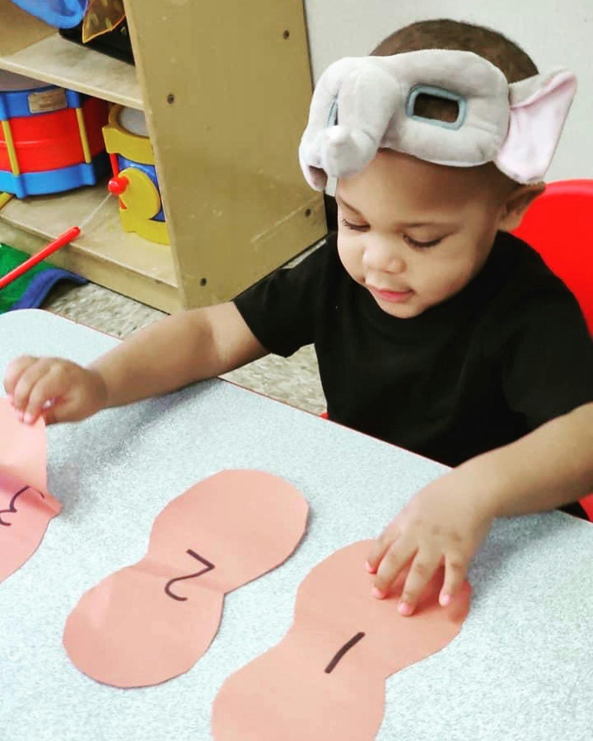 Child wearing an elephant eye mask playing with paper cutouts on a table
