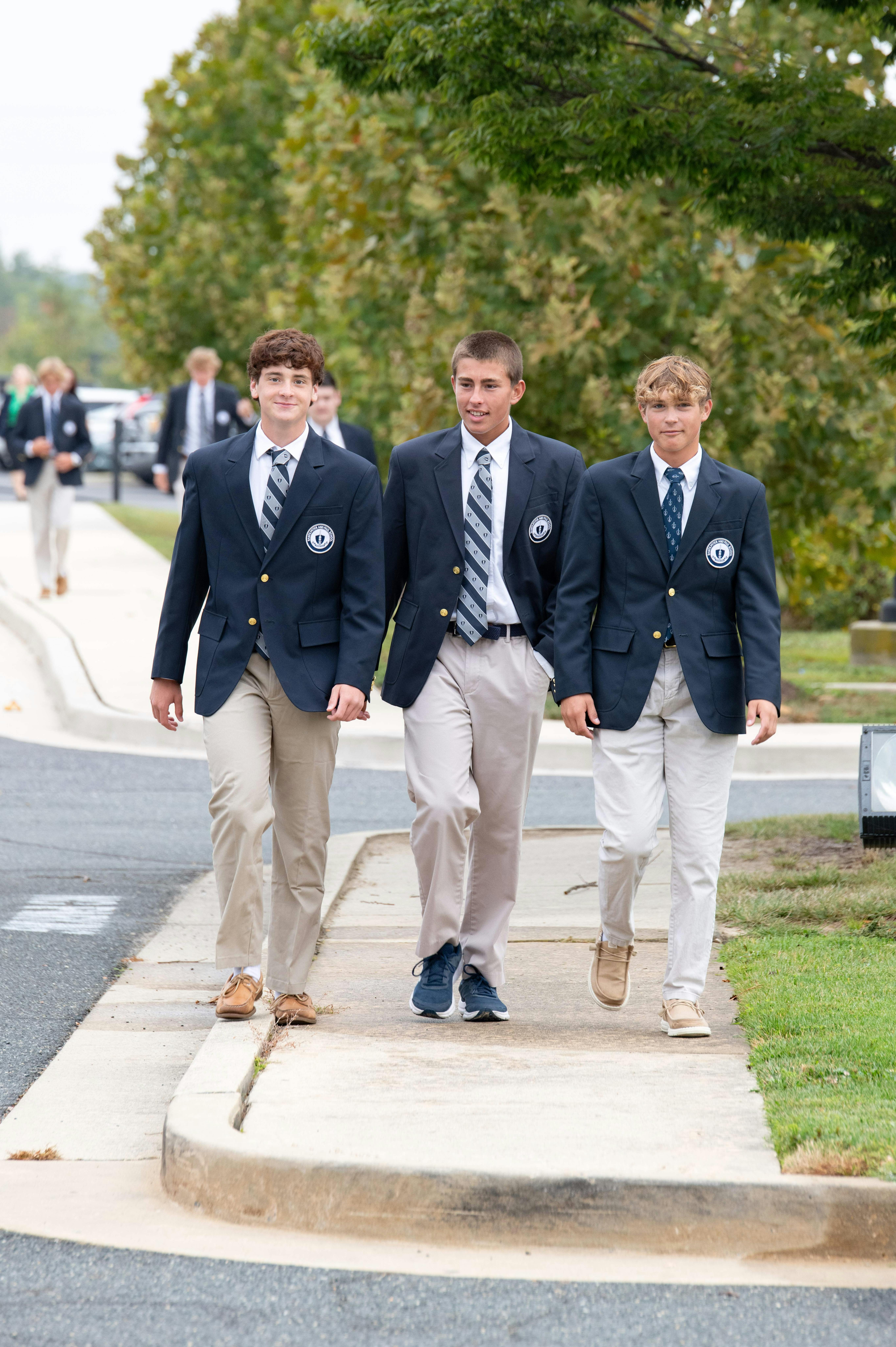 Three teens in blazers and ties walking on a sidewalk