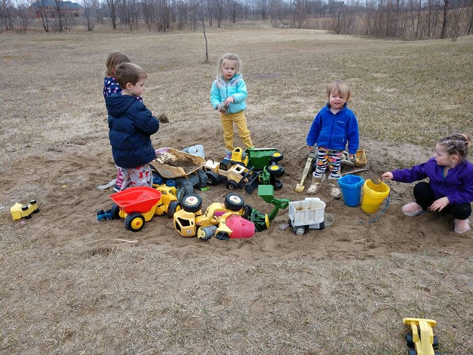 Children playing with toy trucks and buckets in a sand pit
