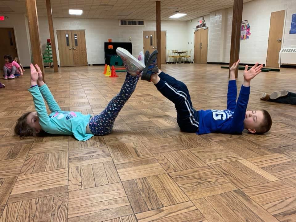 Two children lying on their backs with feet touching in a classroom
