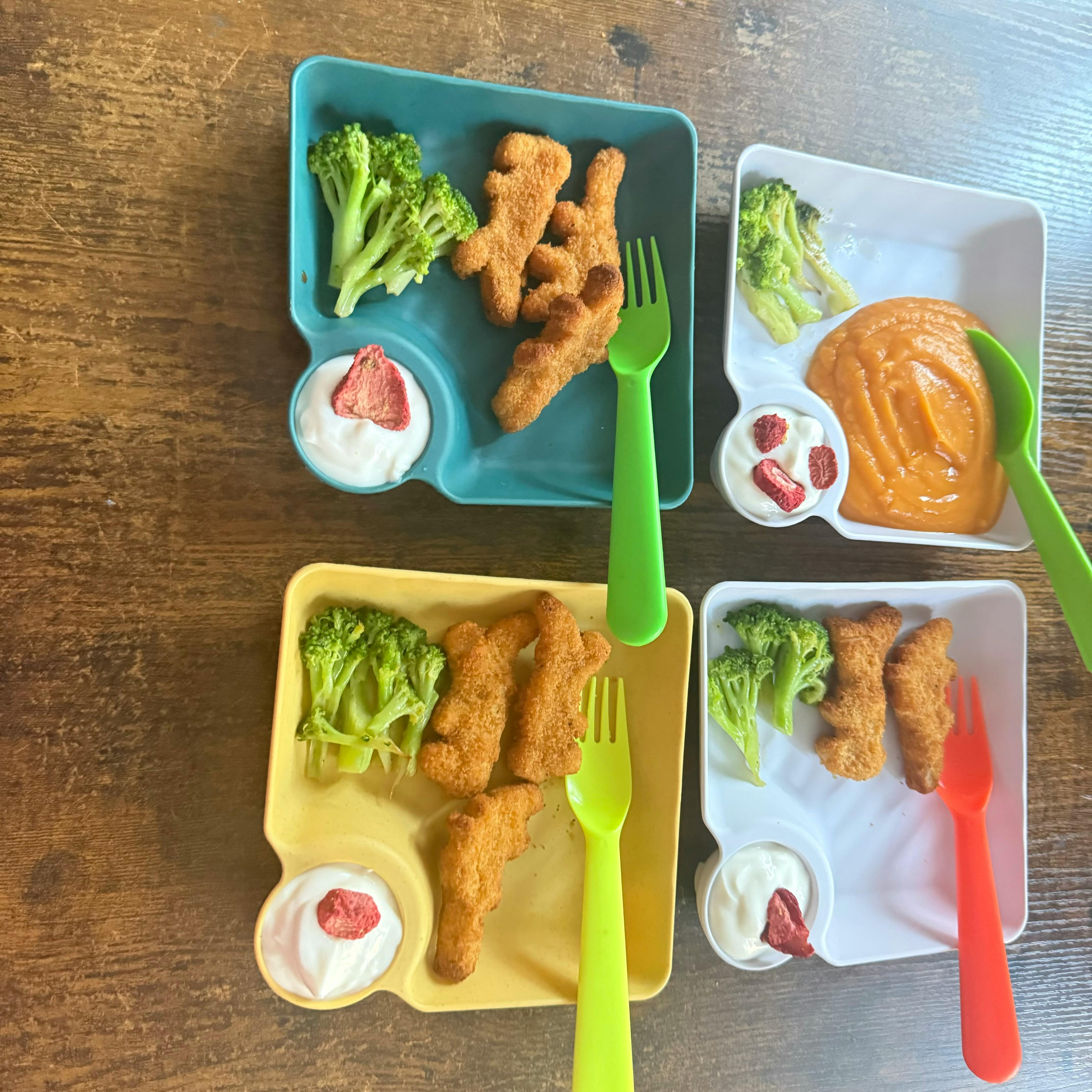 Four plates of food with broccoli, chicken nuggets, and dipping sauce