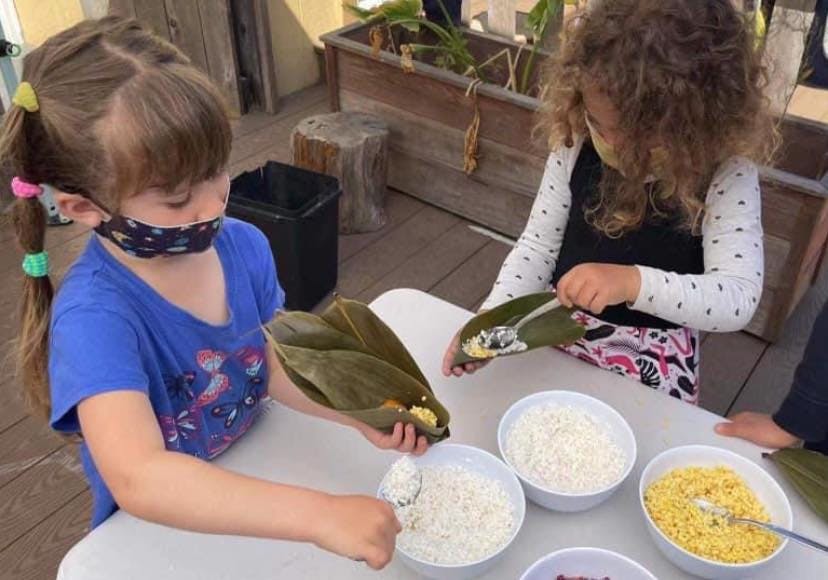 Two children preparing food with leaves and bowls of ingredients