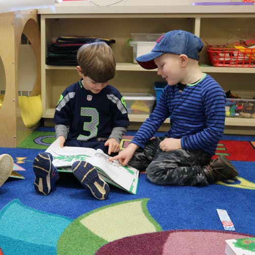 Two children sitting on a rug looking at a book