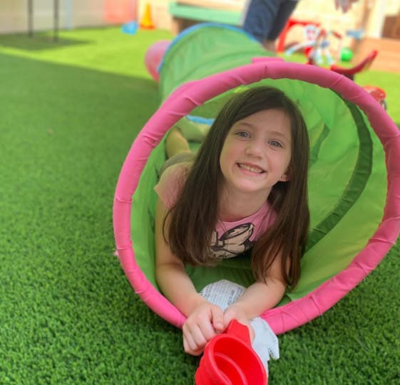 Child in a green and pink play tunnel on artificial grass
