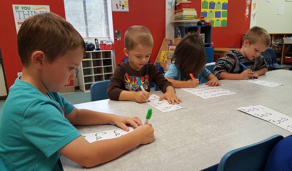 Children writing at a table in a classroom