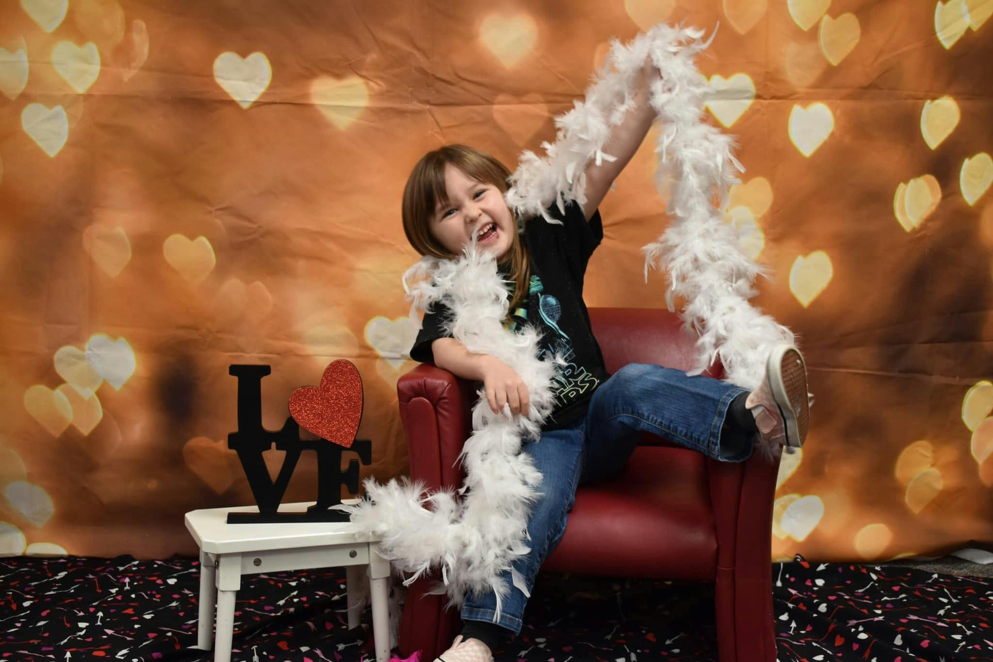 Child sitting in a red chair with a white feather boa