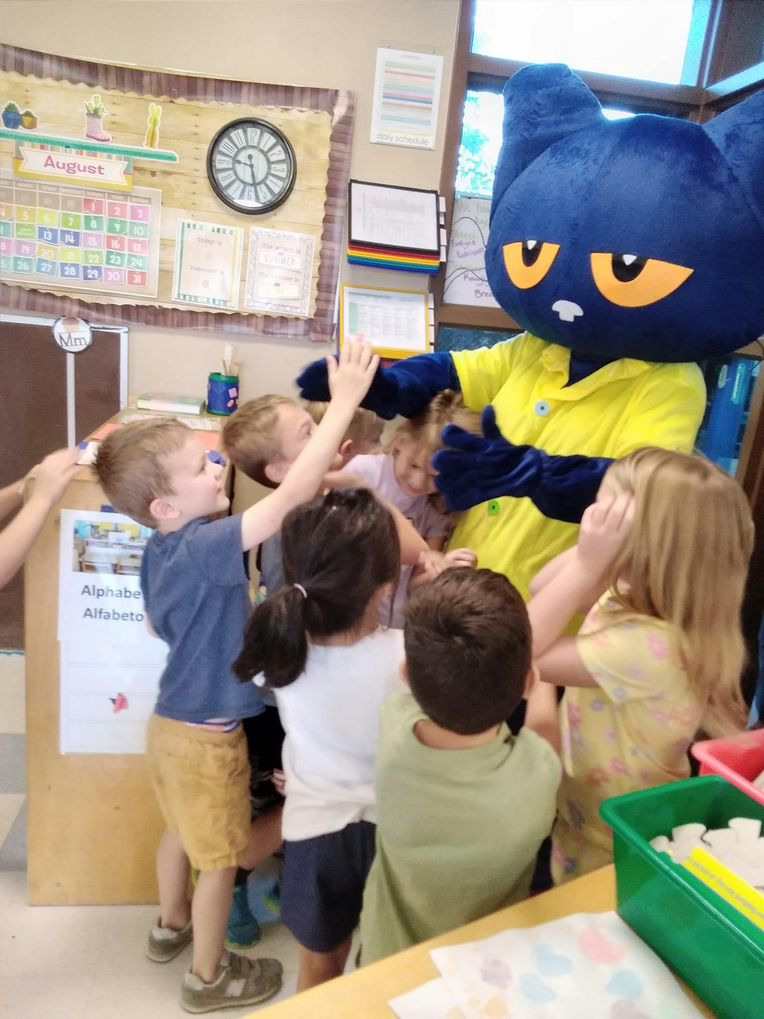Children reaching out to a person in a blue cat mascot costume