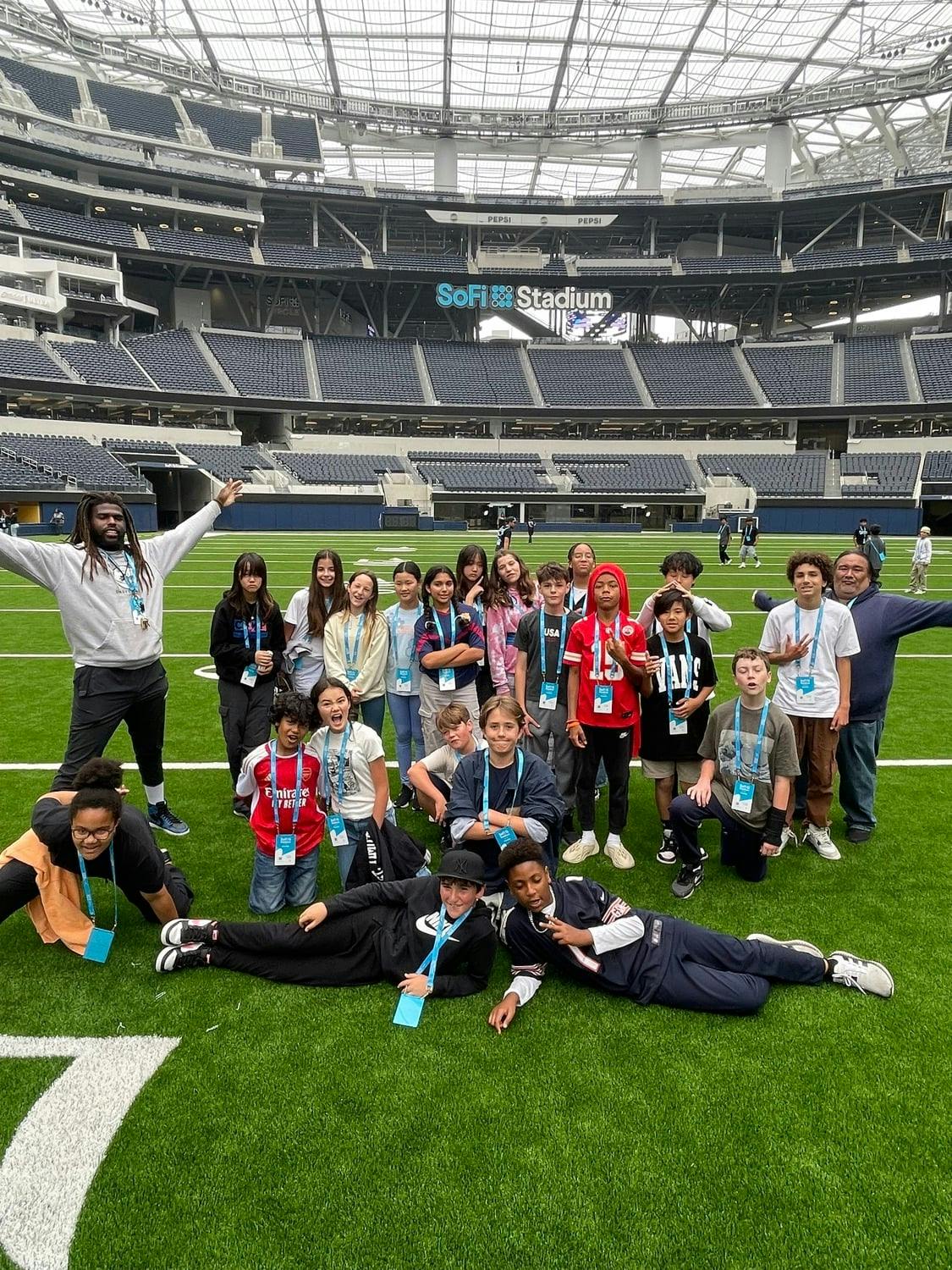 Group of children and adults posing on a football field in a stadium
