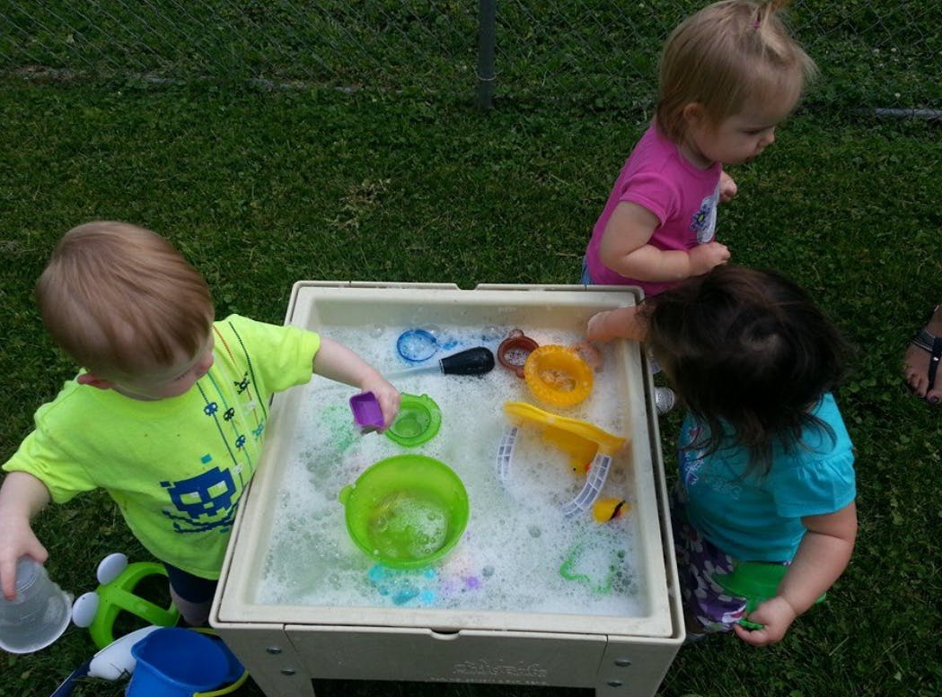 Three children playing with water and toys at a sensory table