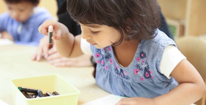 Child holding a crayon over a box of crayons