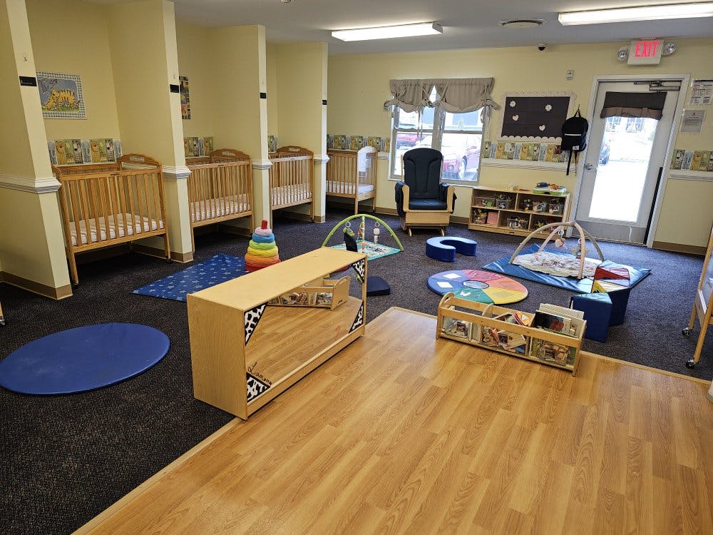 Baby room with cribs along a wall, play mats, and a small bookshelf