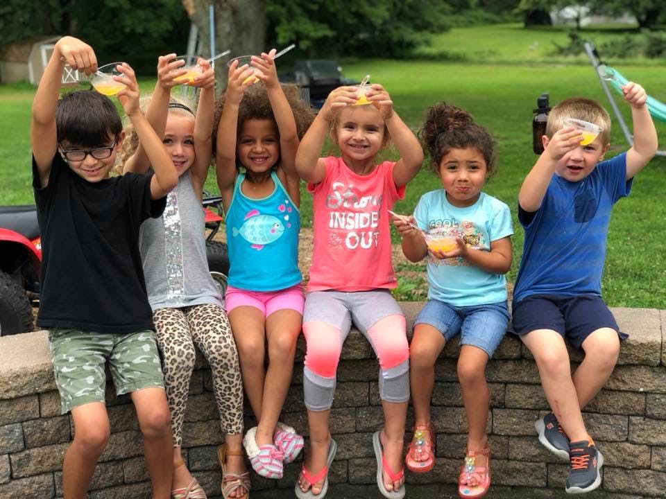 Six children sitting on a stone wall holding up cups