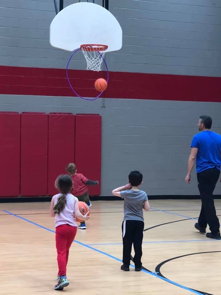 Children and an adult playing basketball in a gym