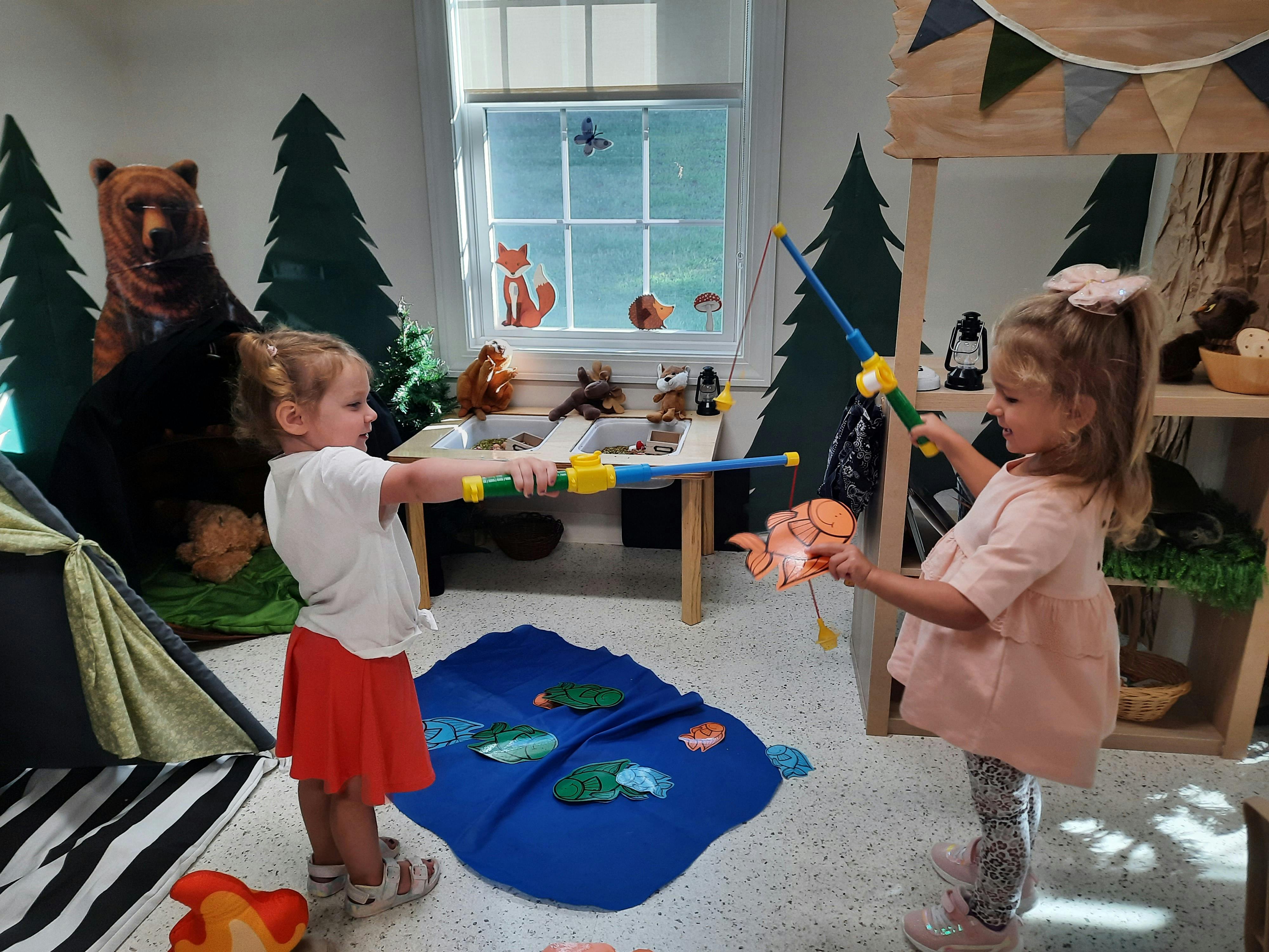 Two children playing with toy fishing rods in a forest-themed room