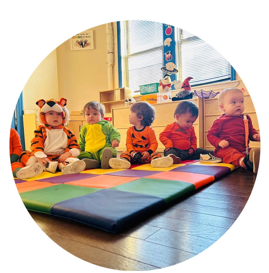 Five children in costumes sitting on a colorful mat
