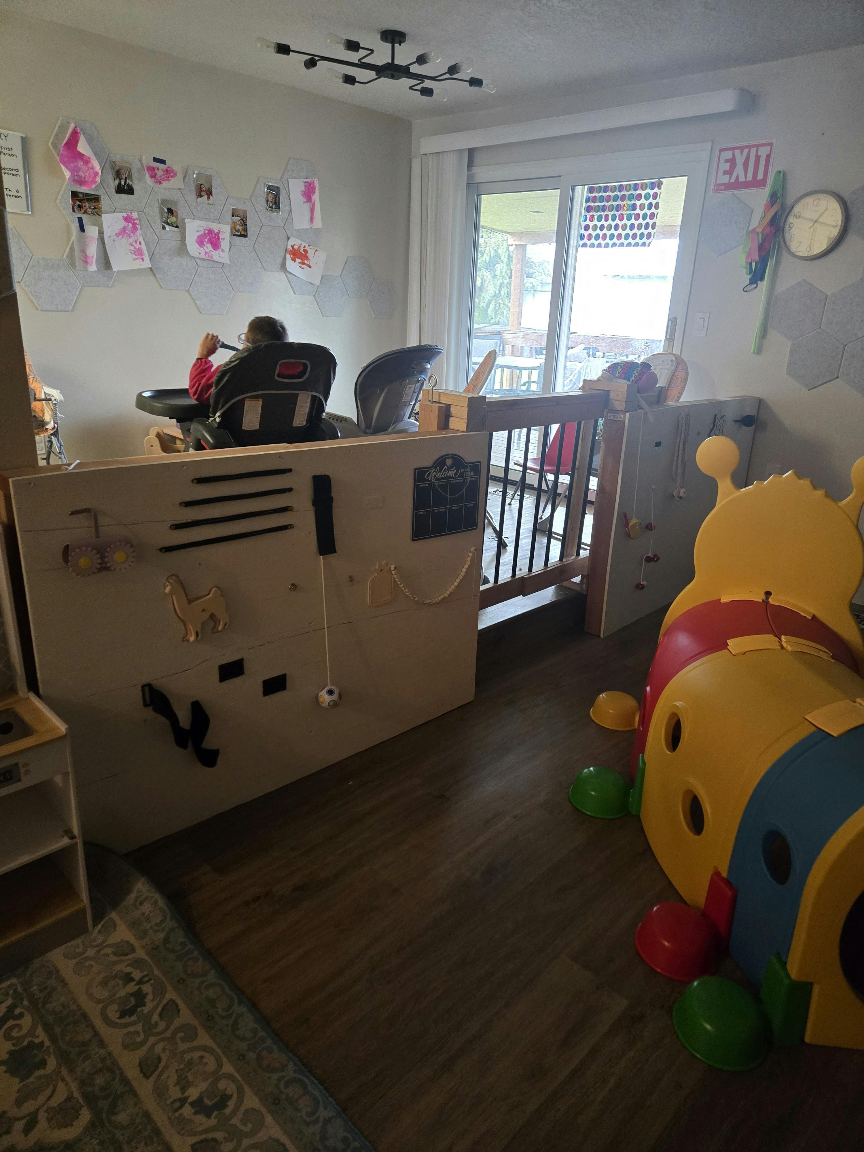 Child sitting in a high chair with an activity wall and play tunnel nearby