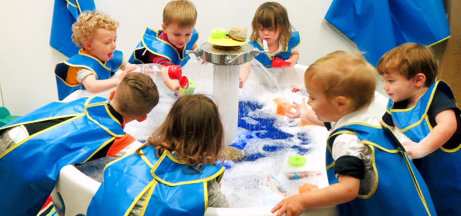 Children in blue smocks playing at a water table