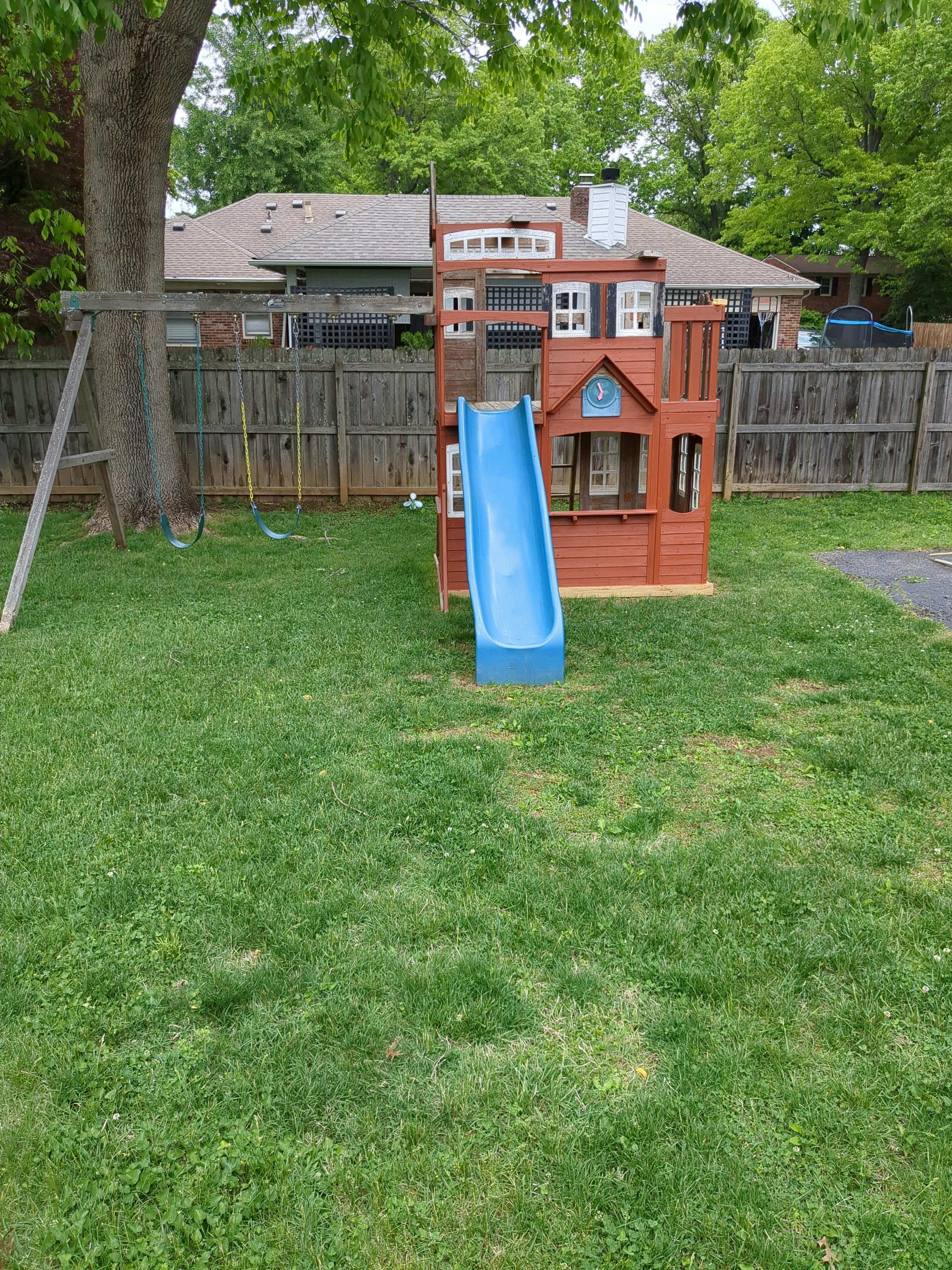 wooden playset with a blue slide in a grassy backyard