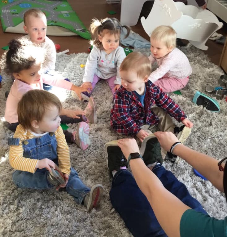 Multiple children sitting on a rug with an adult's legs