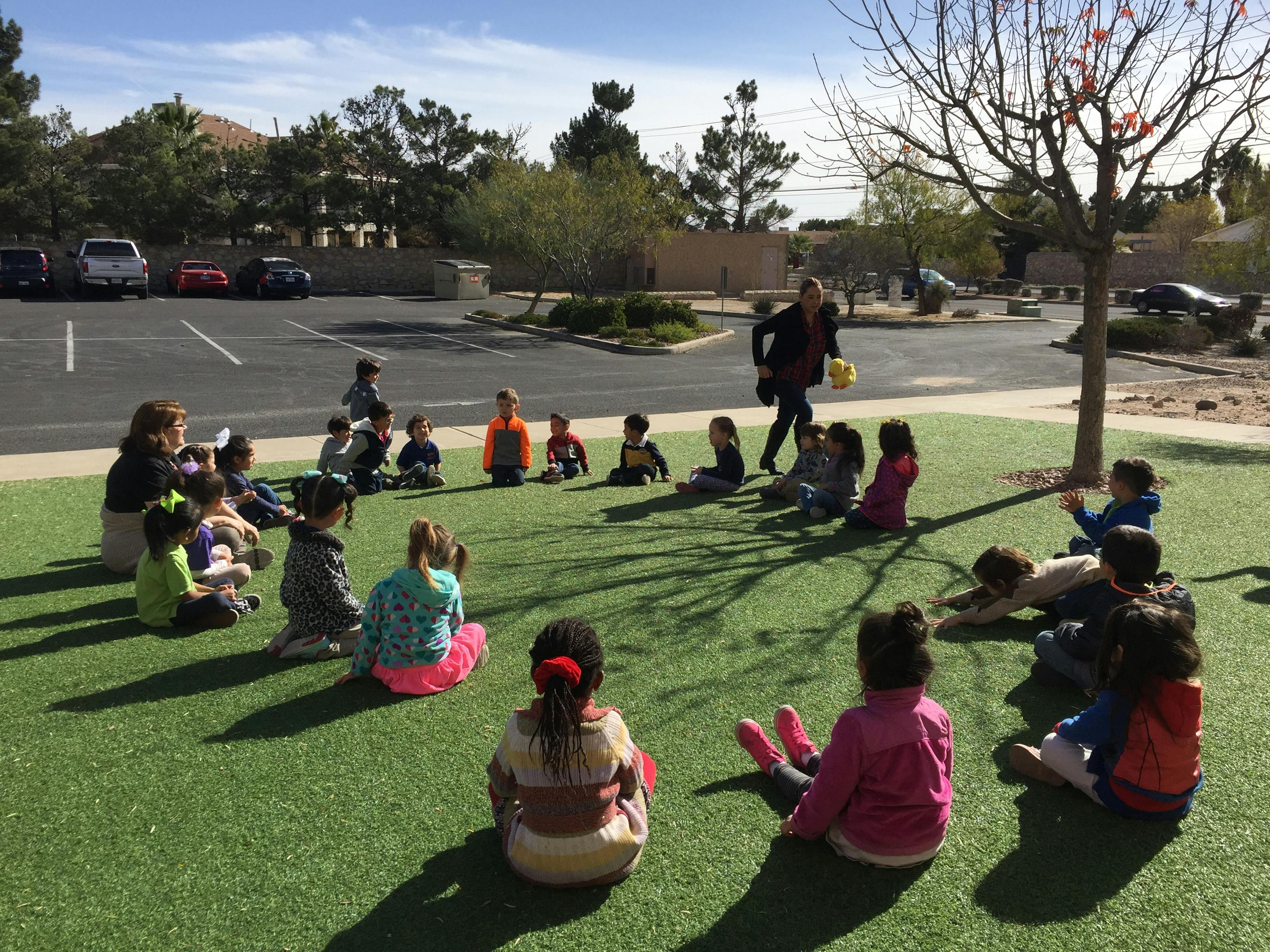 Adult and children sitting in a circle on grass outdoors