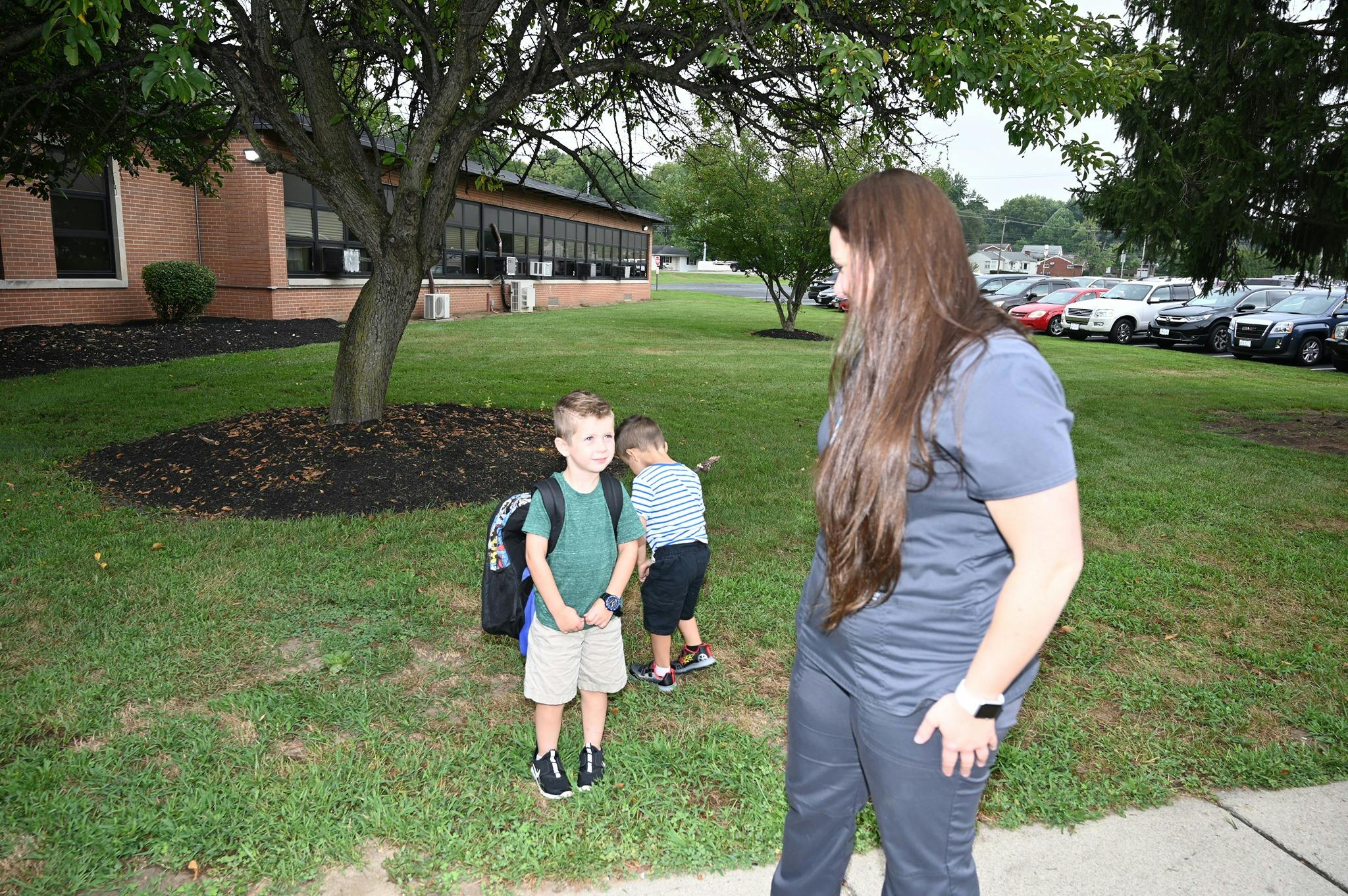 Person standing on grass with two children wearing backpacks
