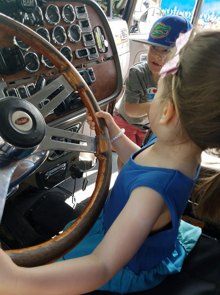 Child holding a steering wheel in a vehicle with another child in the background