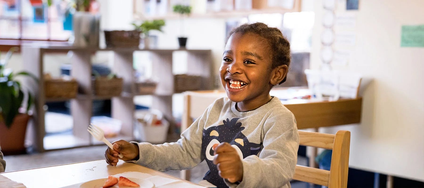 Child at a table holding a fork with a plate of strawberries