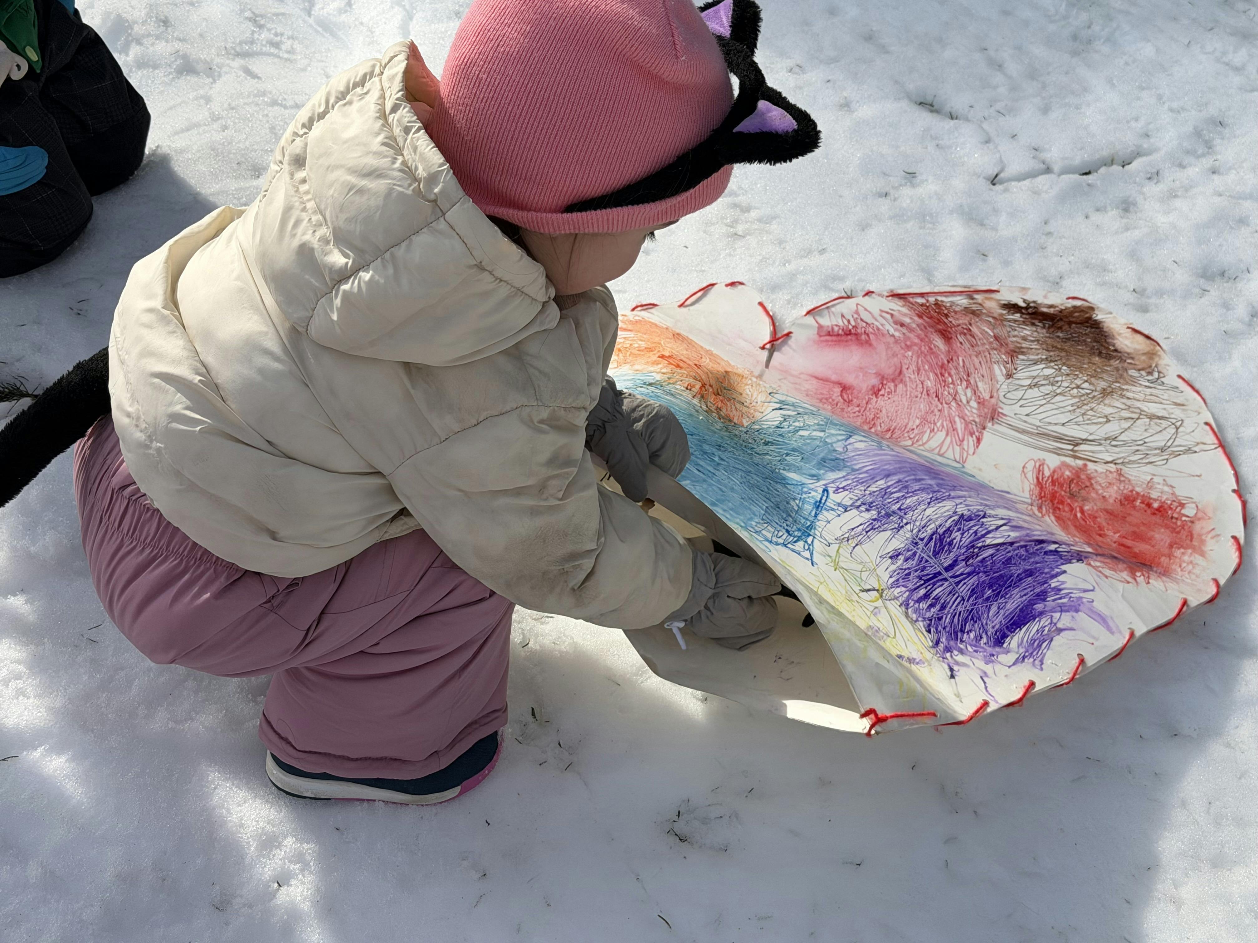 Child in winter gear playing with a decorated cutout in the snow