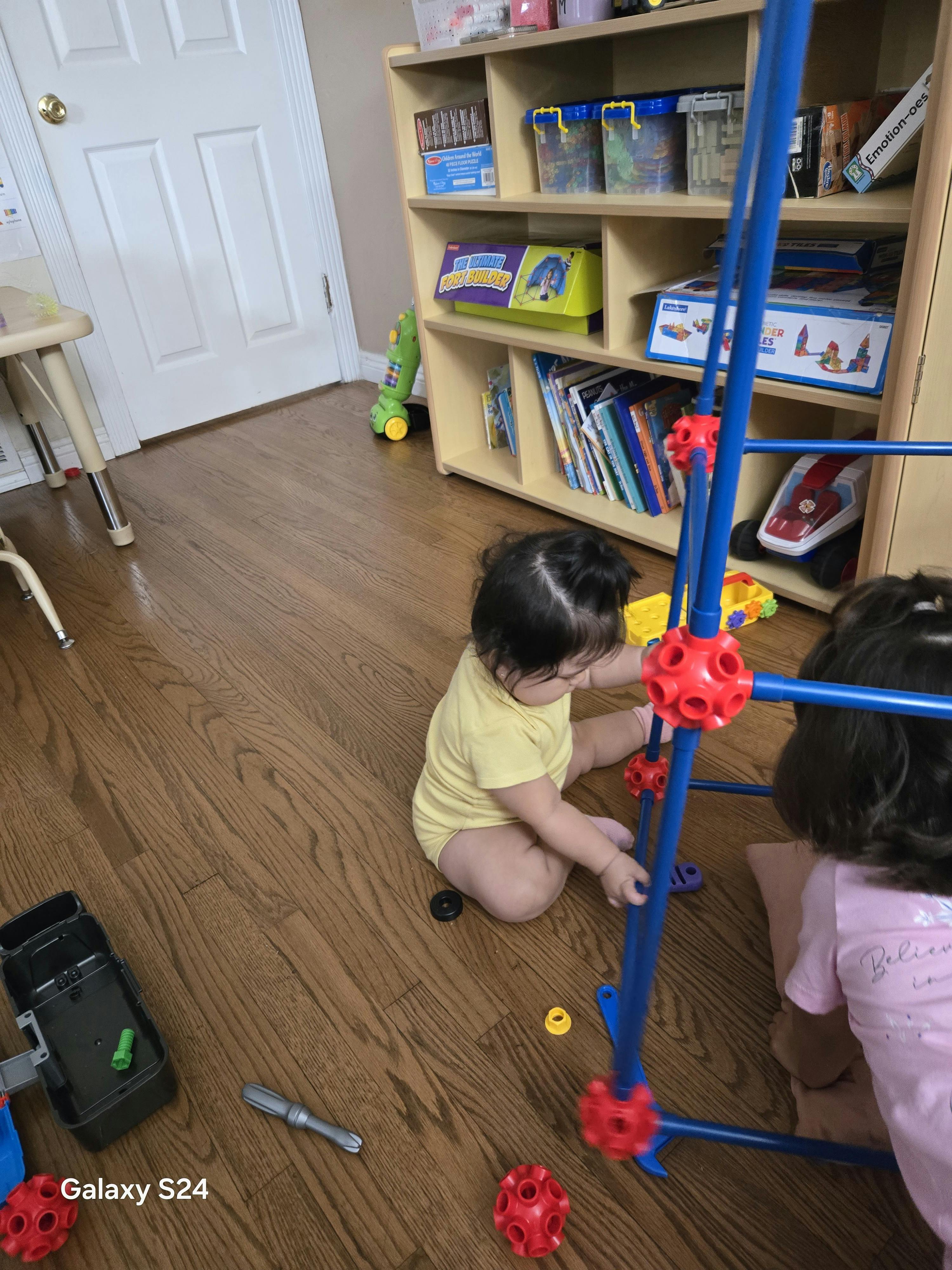 Two children sitting on the floor assembling a plastic fort building set