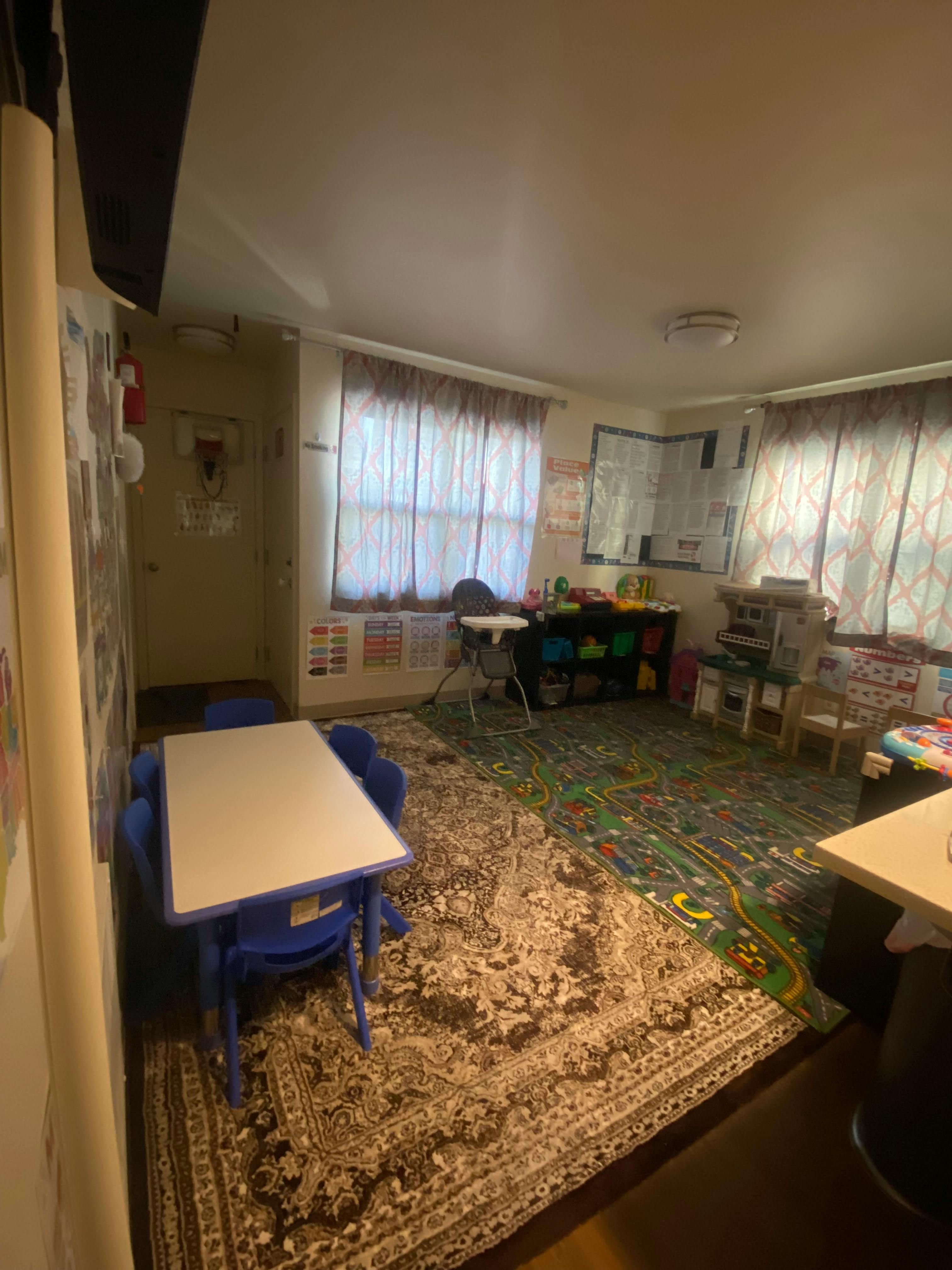 A room with two rugs, a small table with blue chairs, and windows