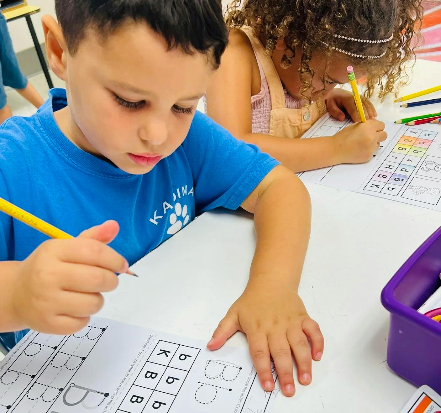 child tracing the letter B on a worksheet in a classroom