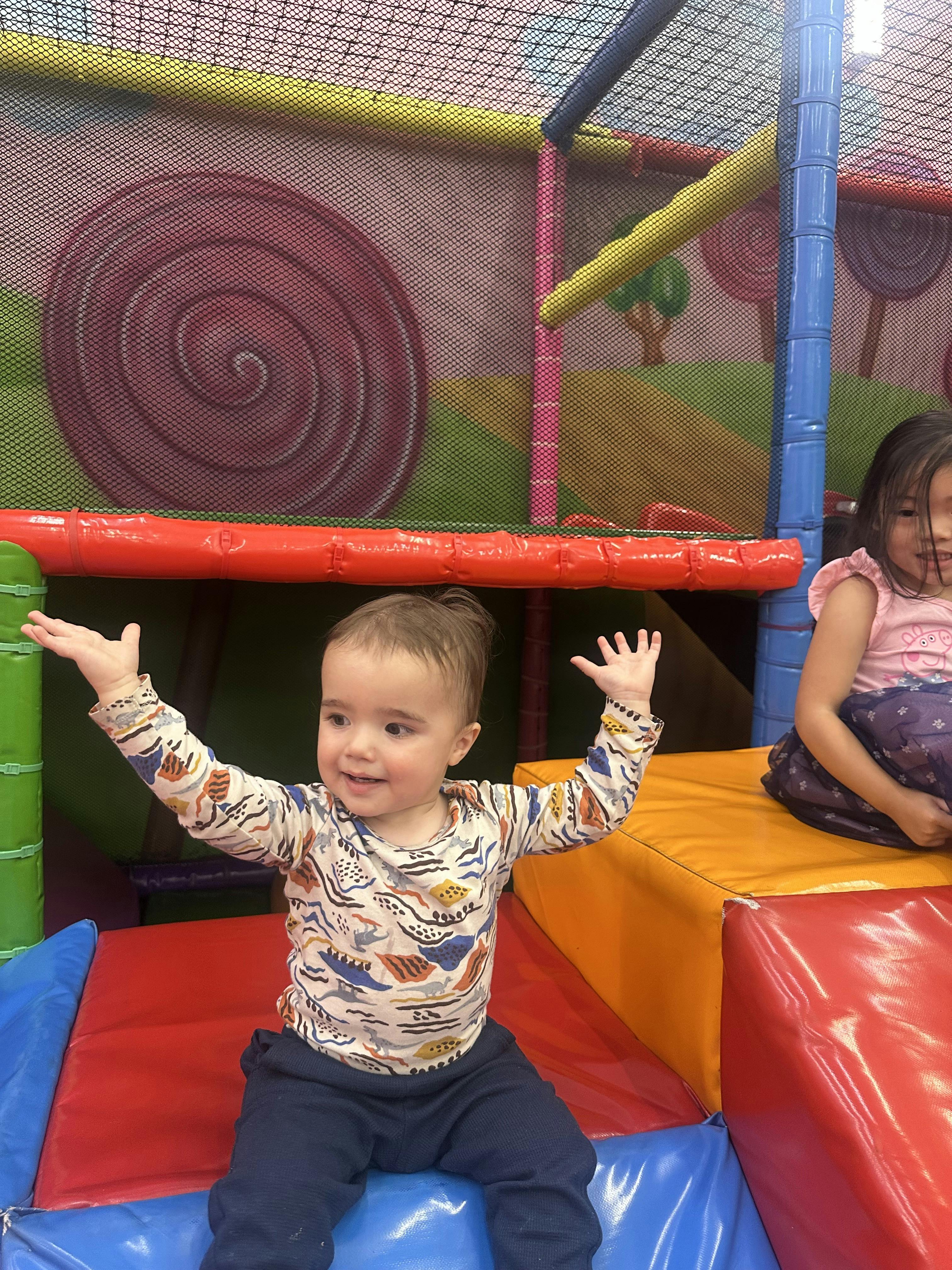Child sitting on soft play equipment with arms raised