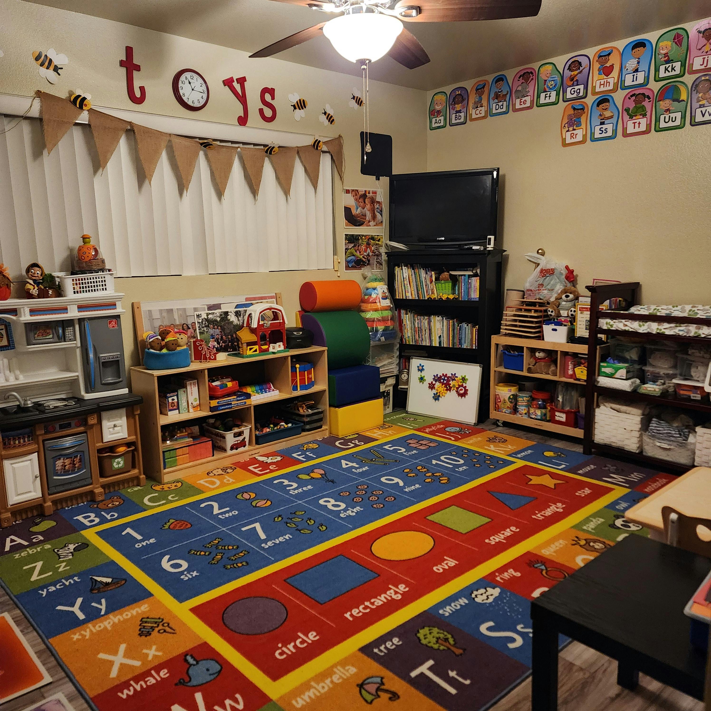 Playroom with a colorful alphabet and numbers rug, shelves with toys and books