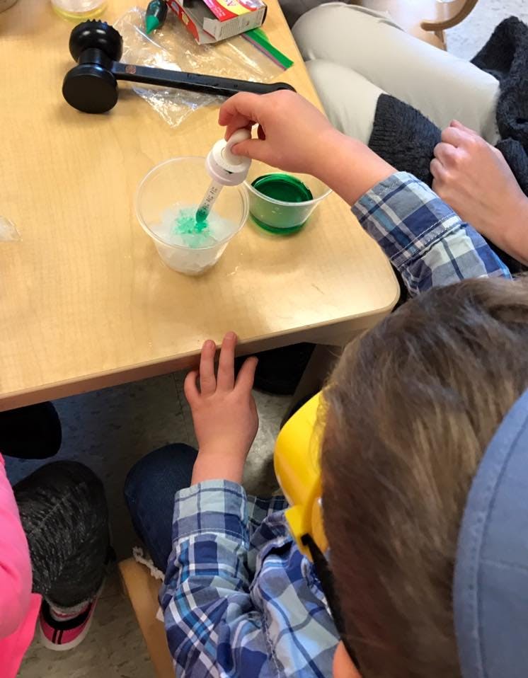 Child using a dropper to add green liquid to a cup of white material