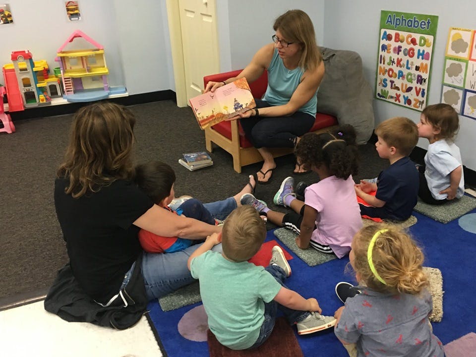 Two people reading to a group of children in a classroom