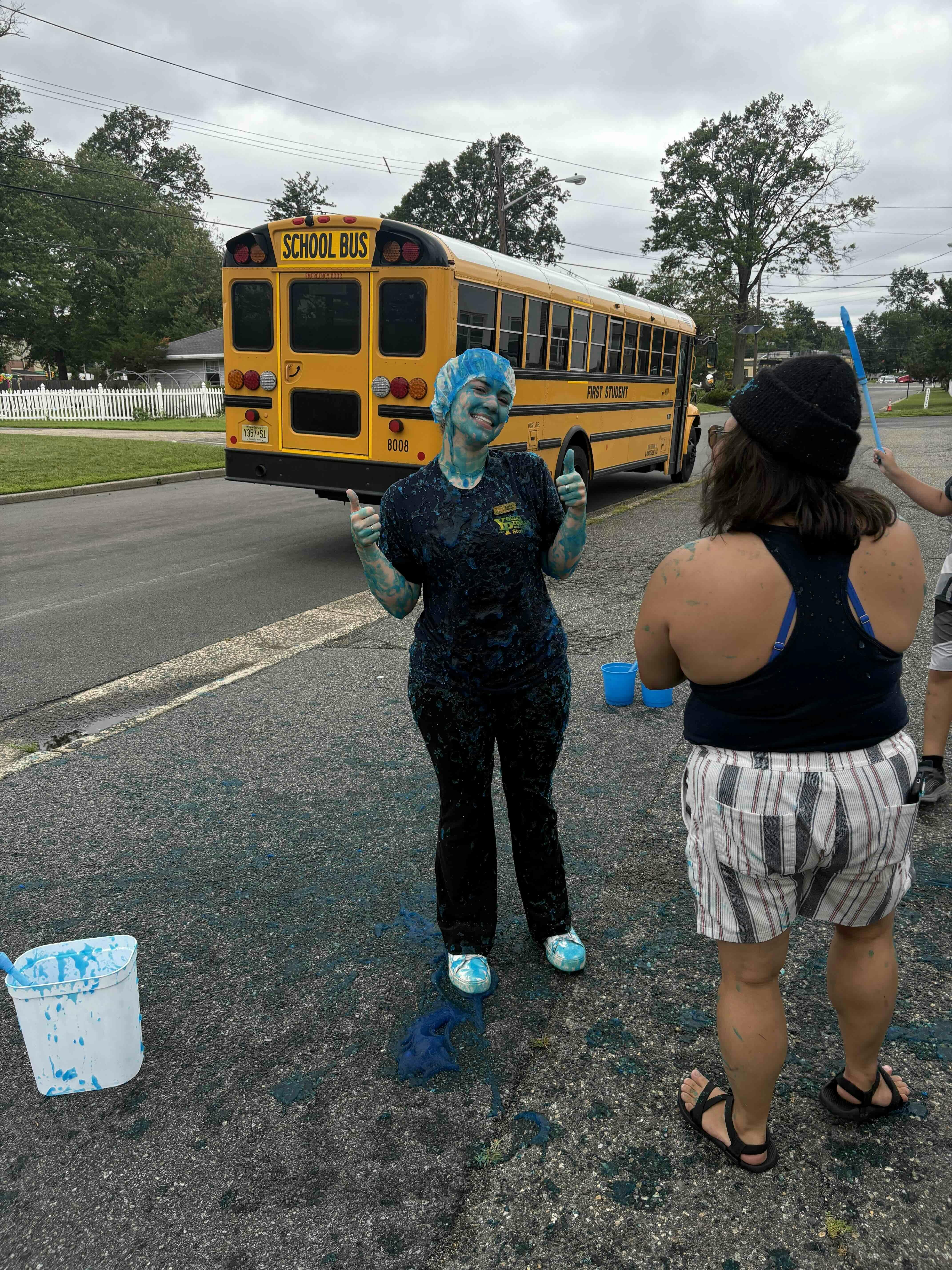 Person covered in blue paint giving thumbs up in front of a school bus