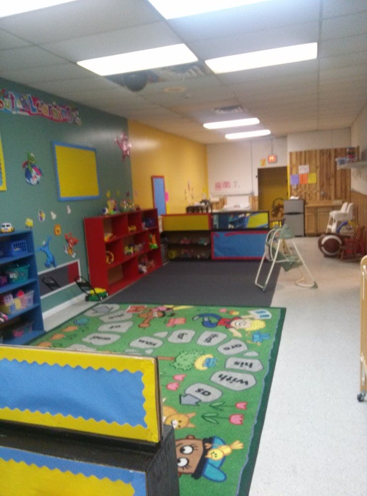 A colorful classroom with a green rug, shelves, and various learning materials