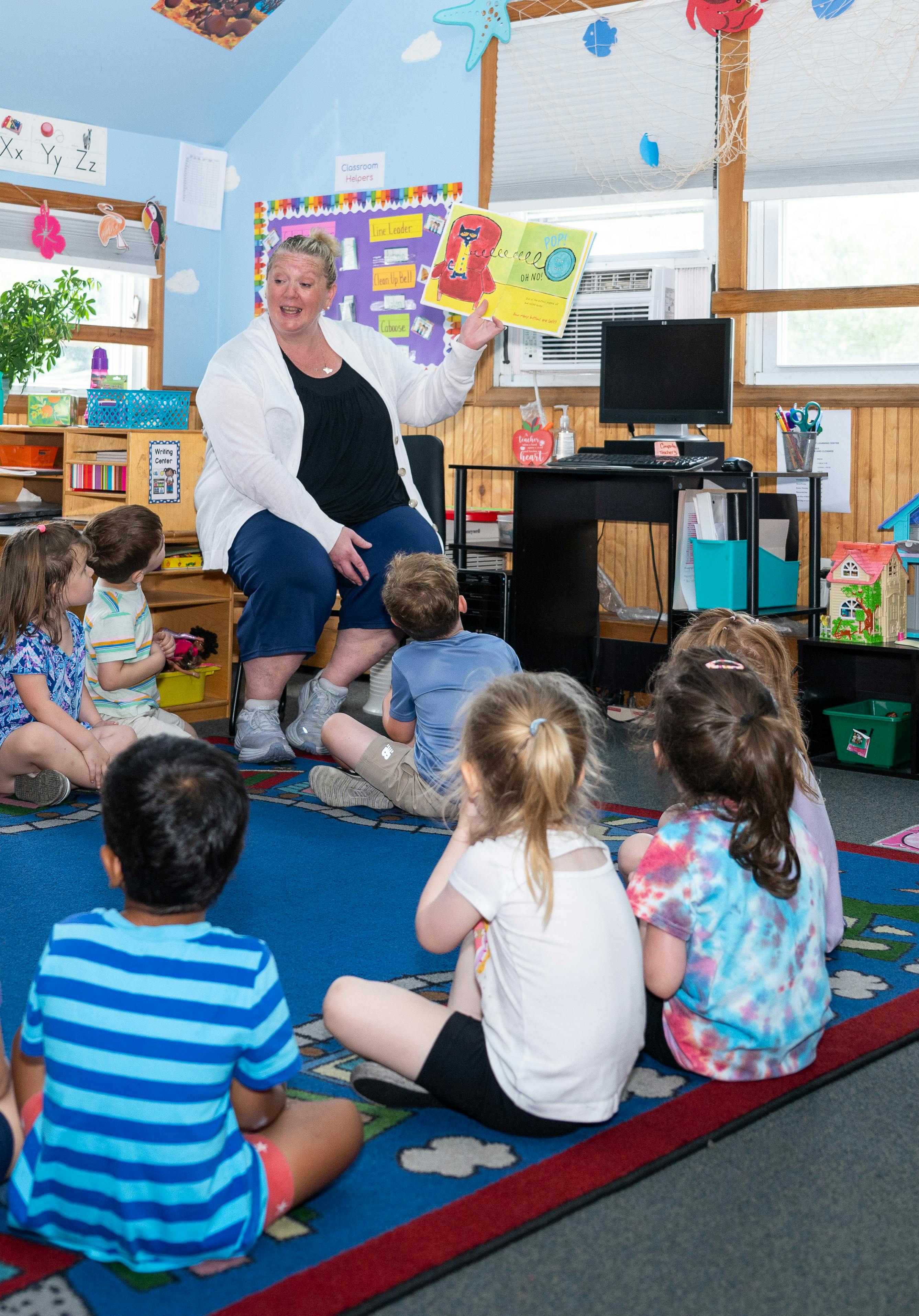 Person reading a book to a group of children in a classroom