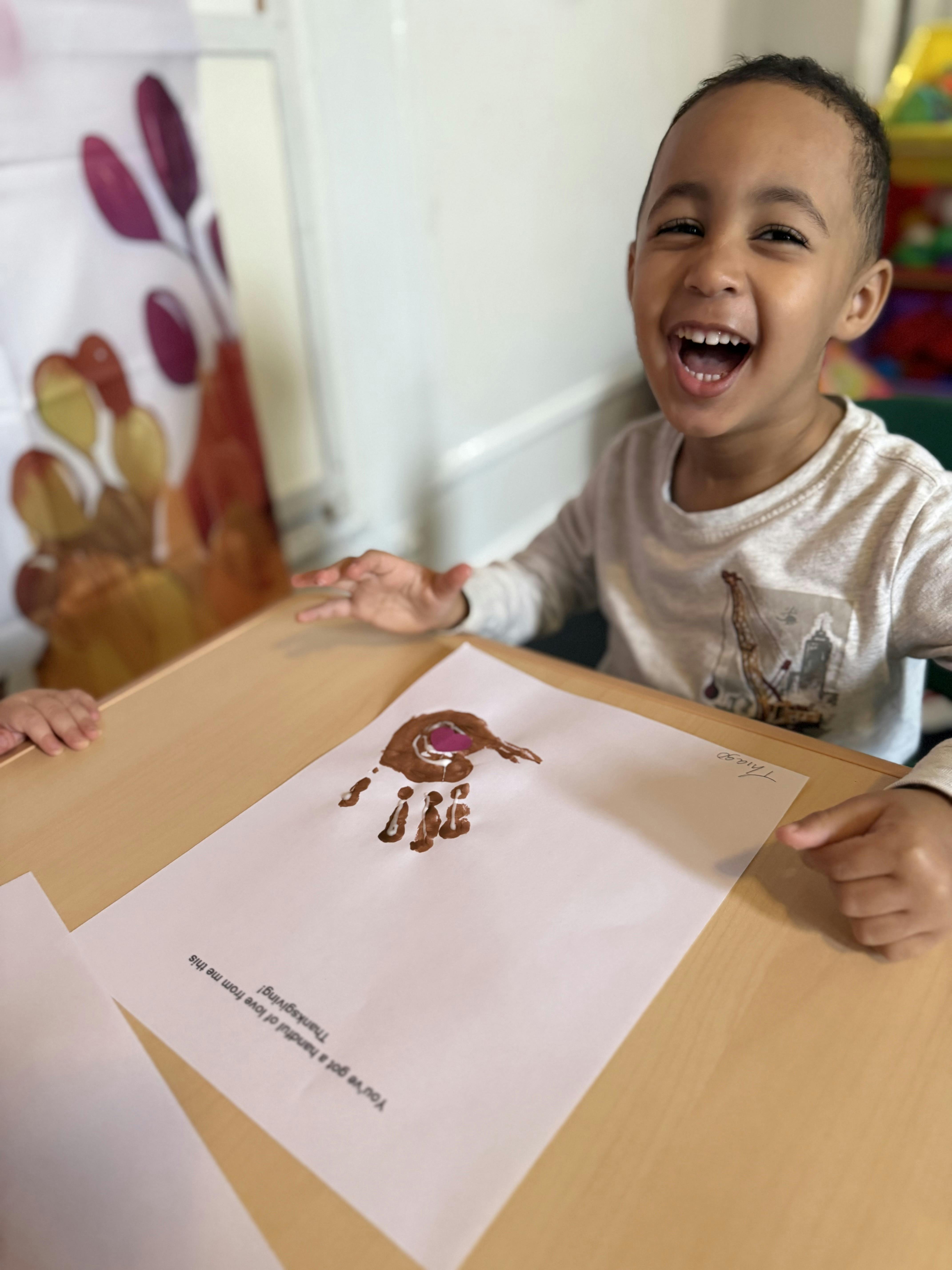 Child smiling at a table with a handprint craft