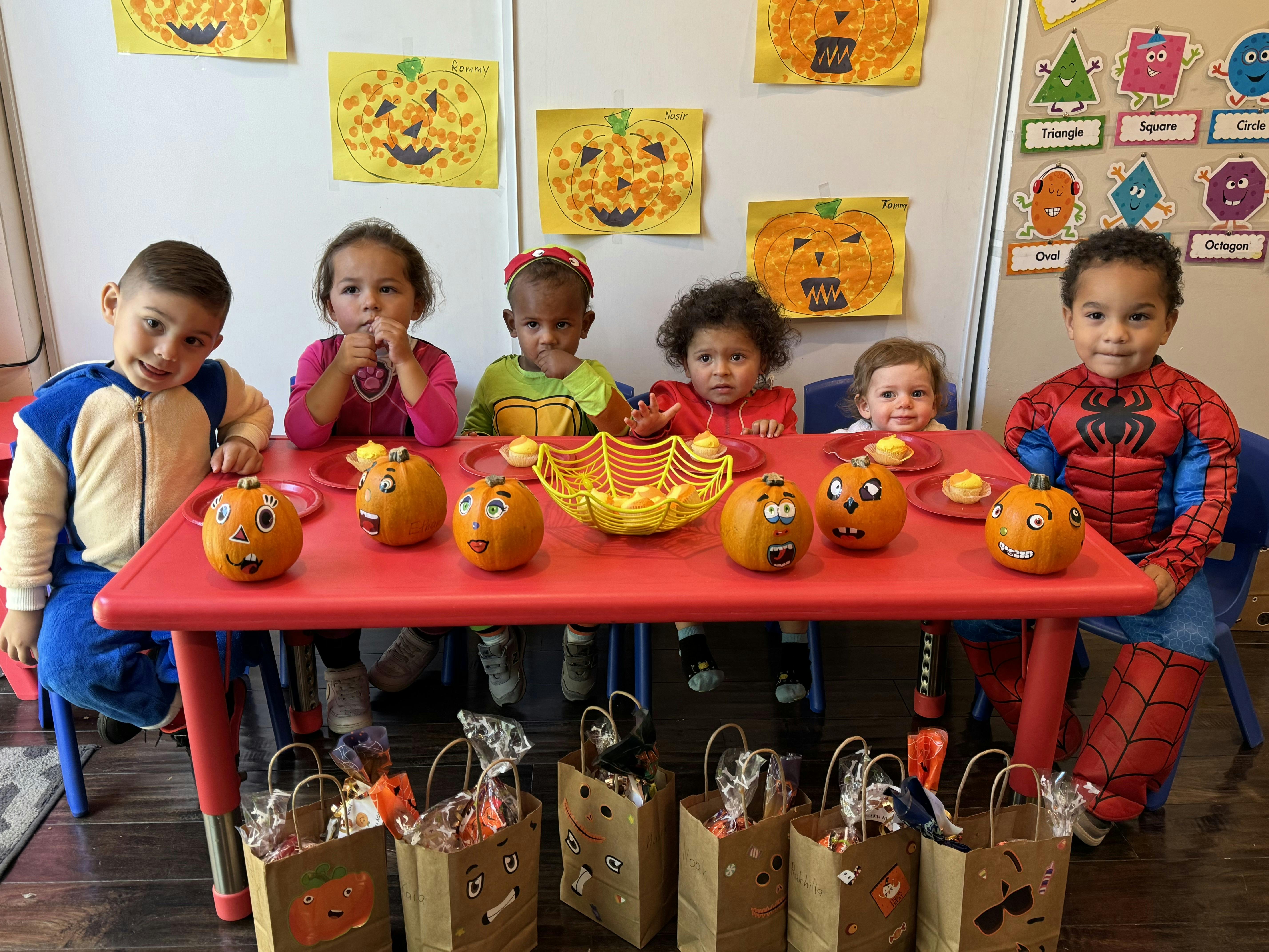 Children sitting at a table with decorated pumpkins and gift bags