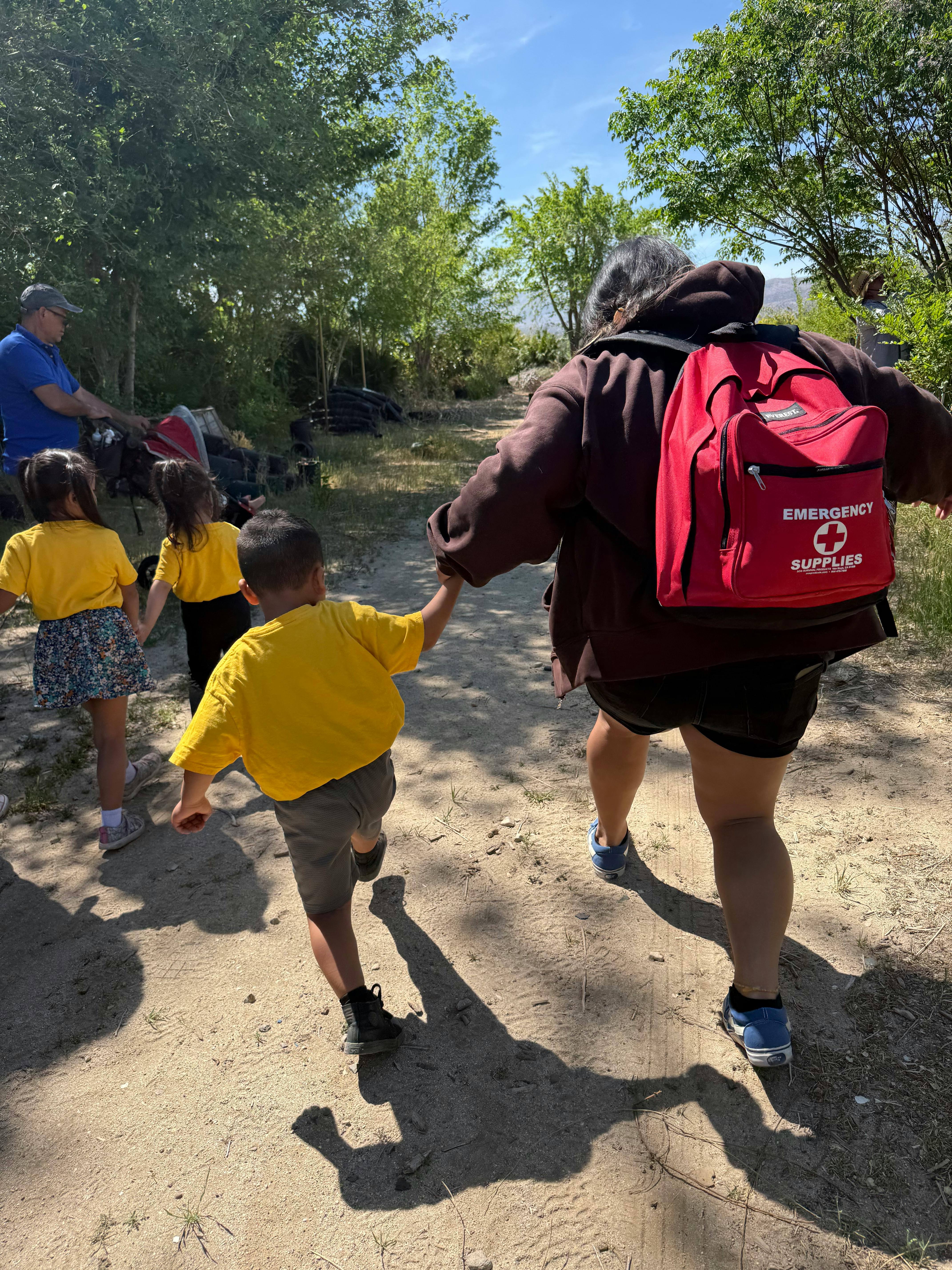 Person with red emergency backpack holding hands with children on a dirt path