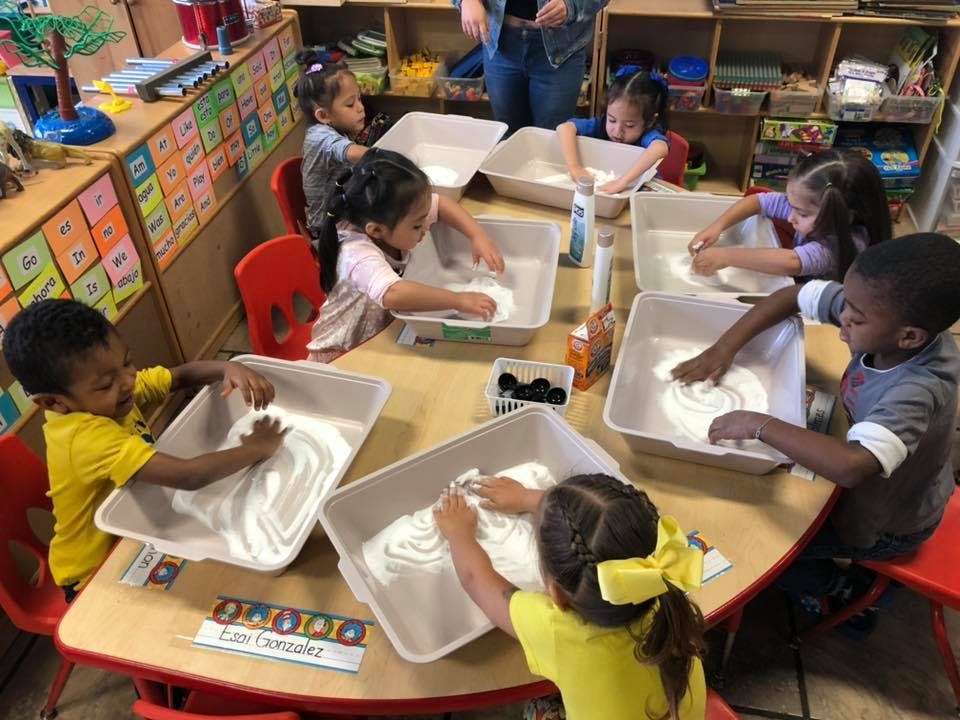 Children playing with sensory bins at a table in a classroom