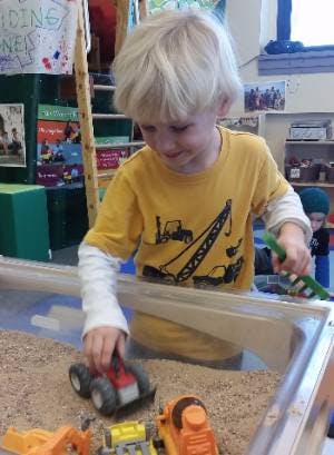 Child playing with toy trucks in a sand table