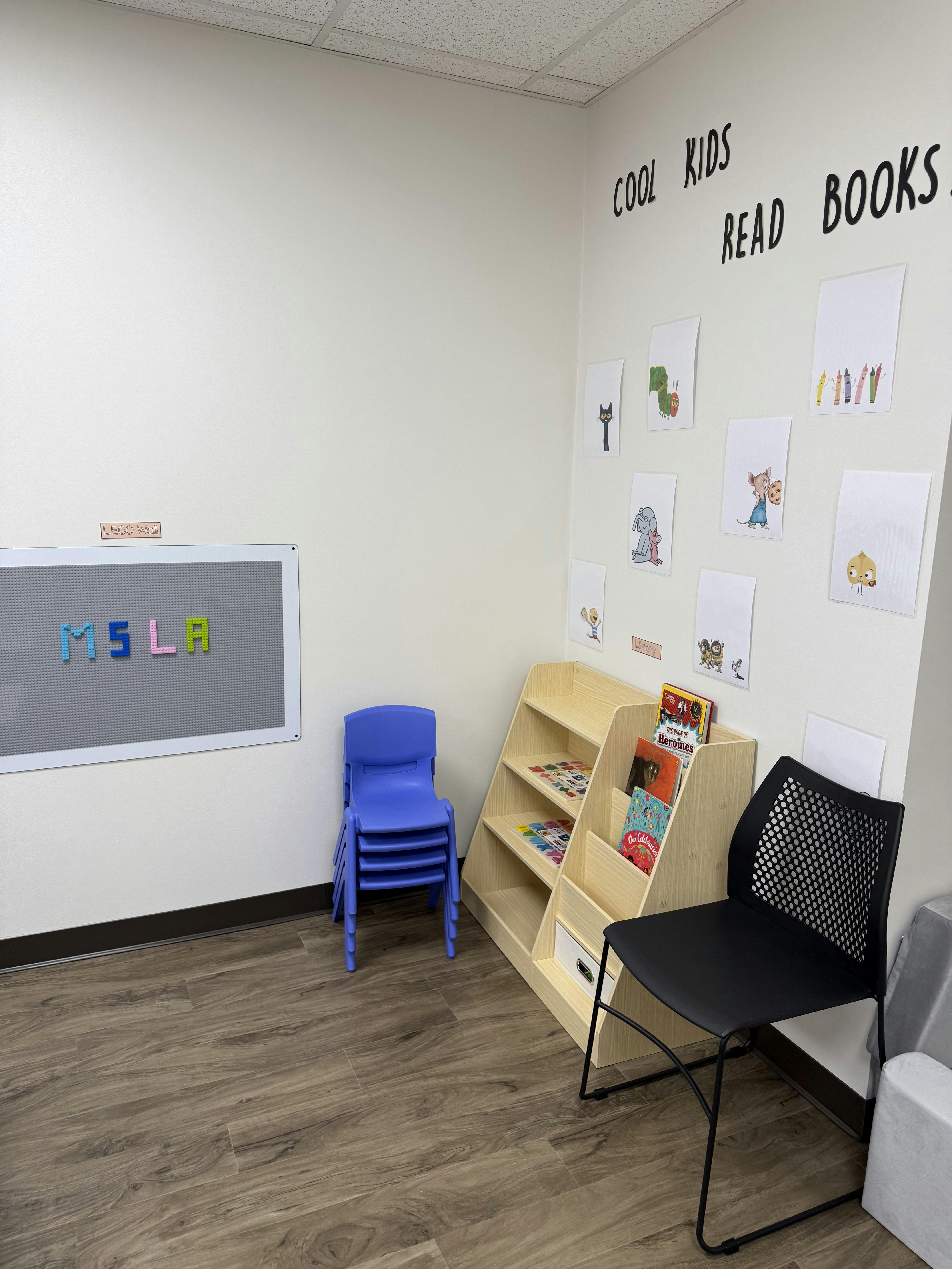 Classroom with a whiteboard, stacked chairs, and bookshelves with "Cool Kids Read Books" on the wall