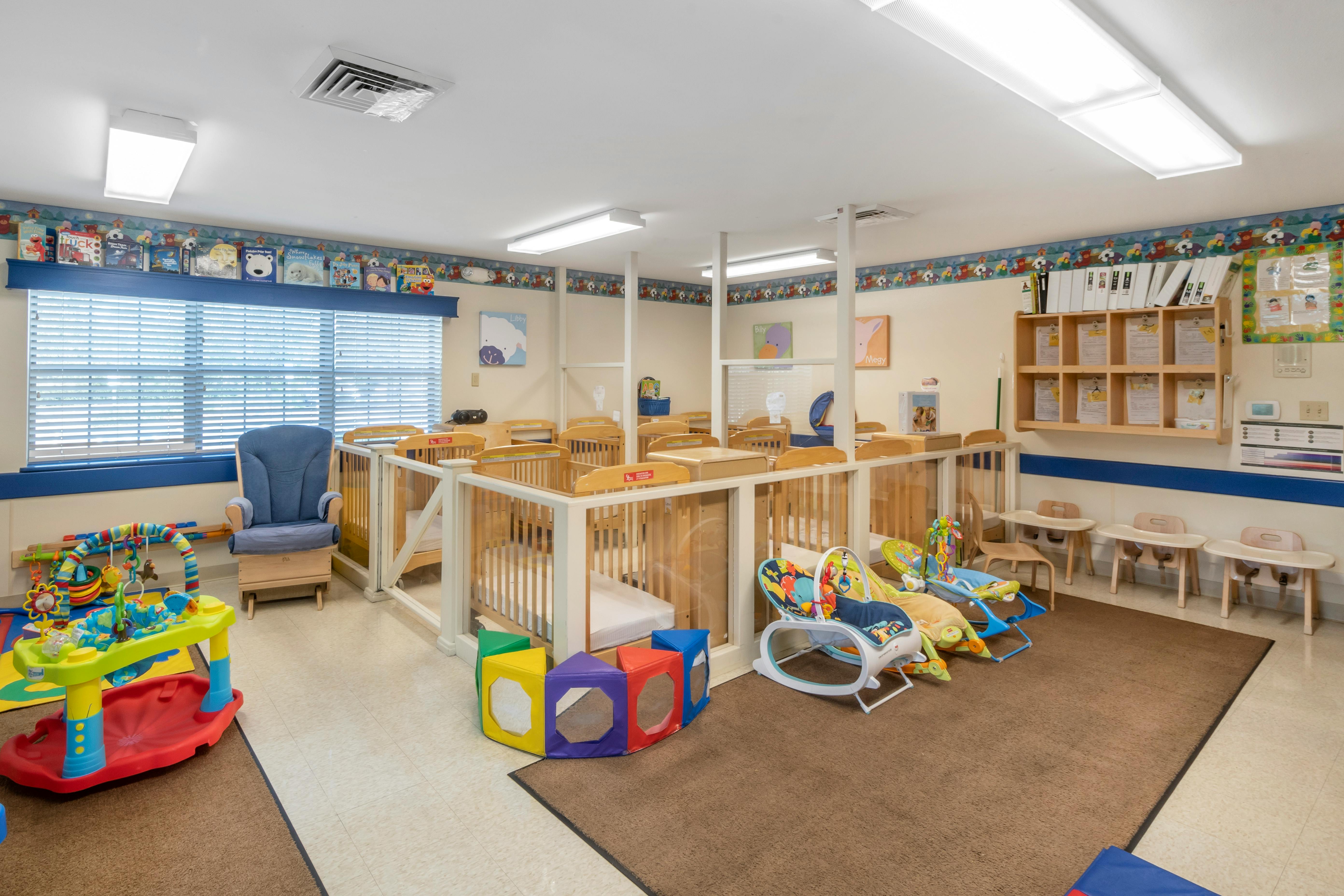 Rows of wooden cribs in a room, with play equipment on a rug