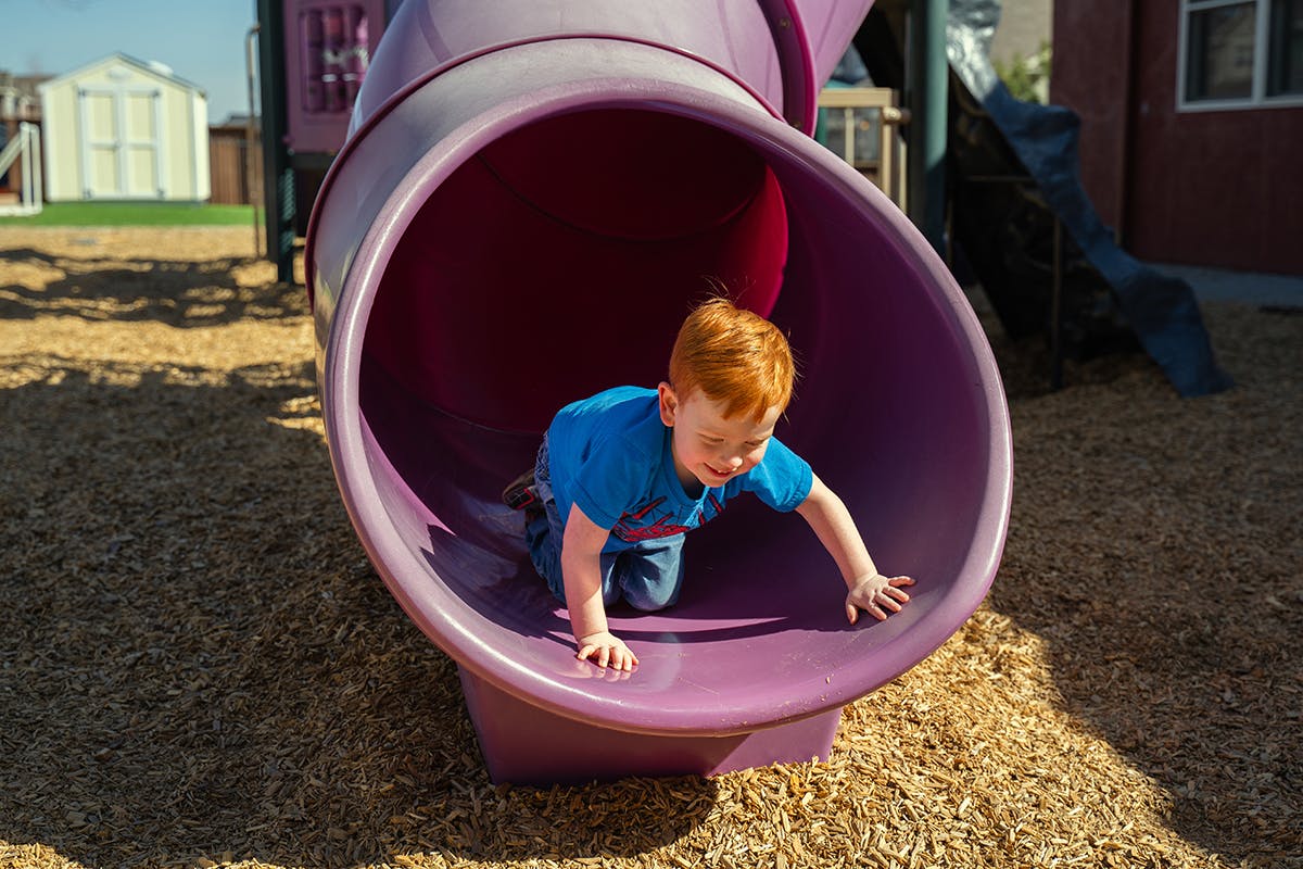 Child crawling out of a purple tunnel slide