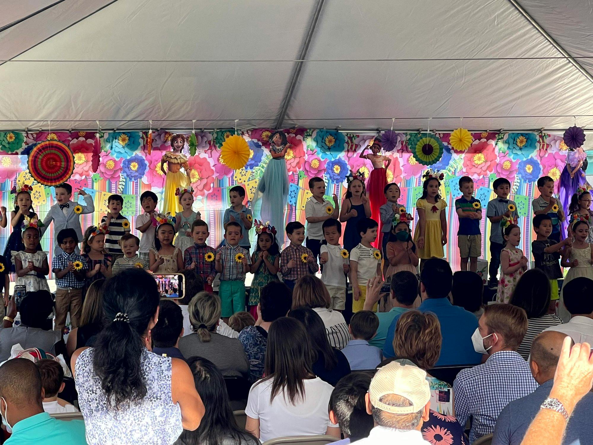 Group of children singing on stage in front of a floral backdrop