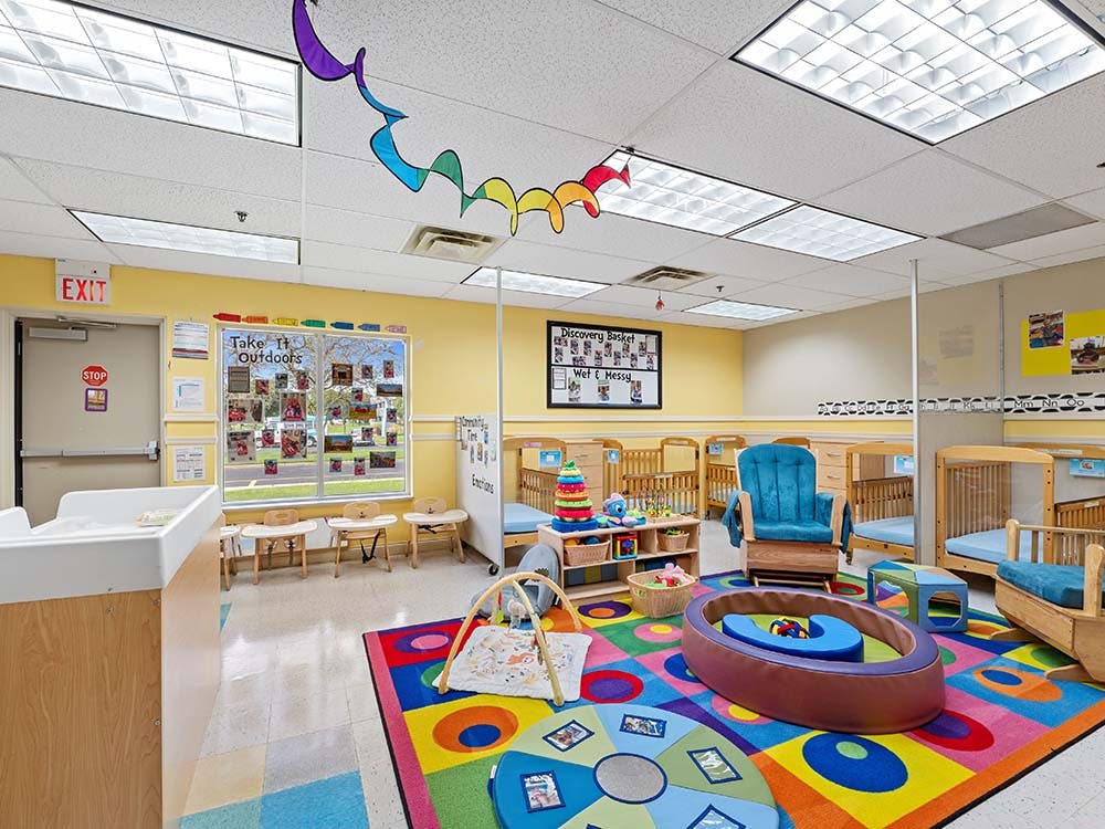 Classroom with colorful rug, play area, cots, and changing station