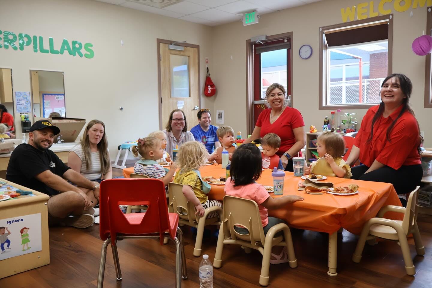 Adults and children gathered around tables eating food in a classroom