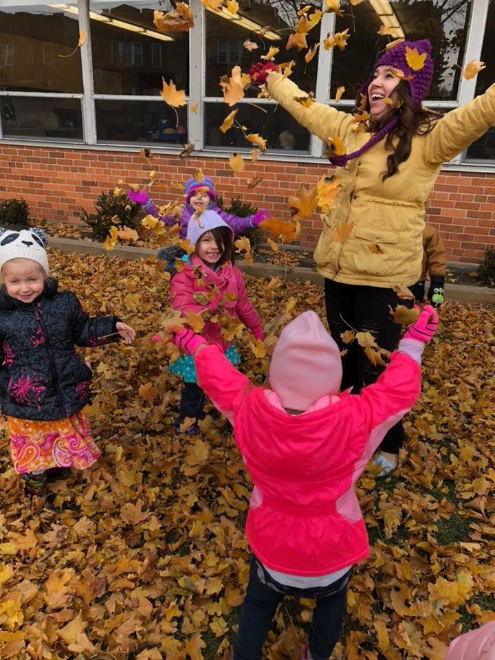 Adult and children playing in falling leaves outdoors
